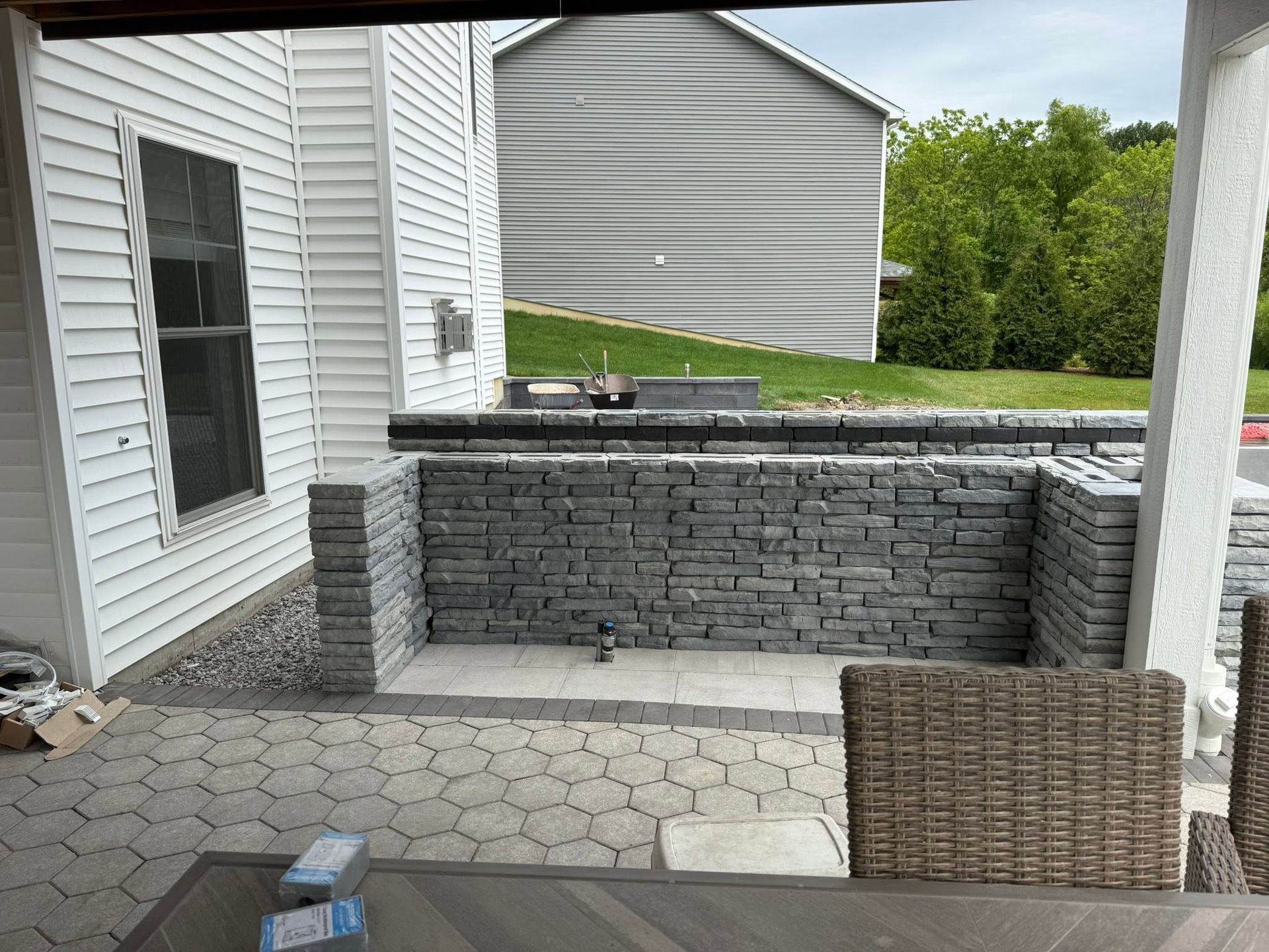 Outdoor patio with gray stone grill island, white siding, and wicker chair on a paved deck