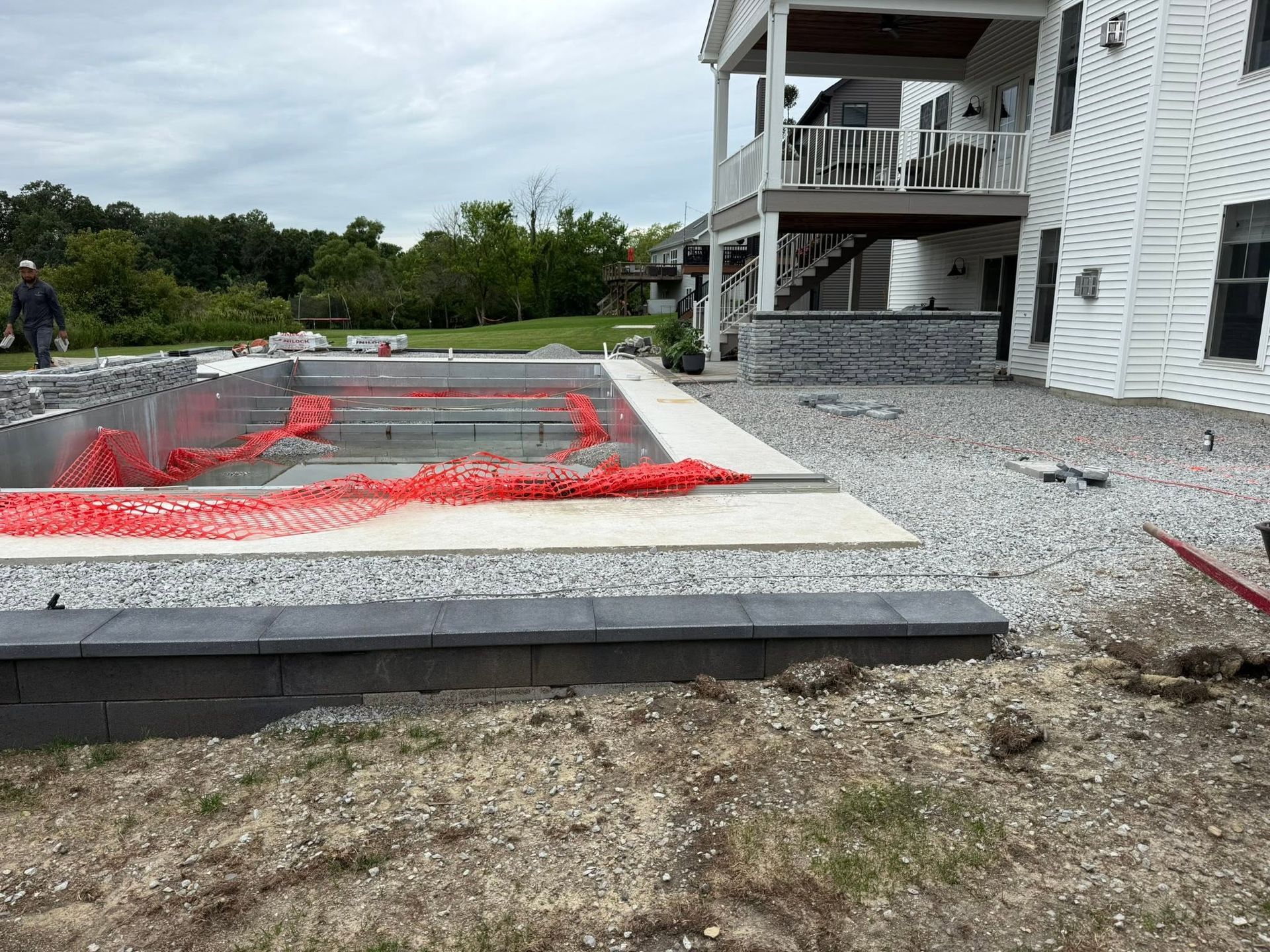House exterior with gravel yard and a red-fenced in-ground pool under construction