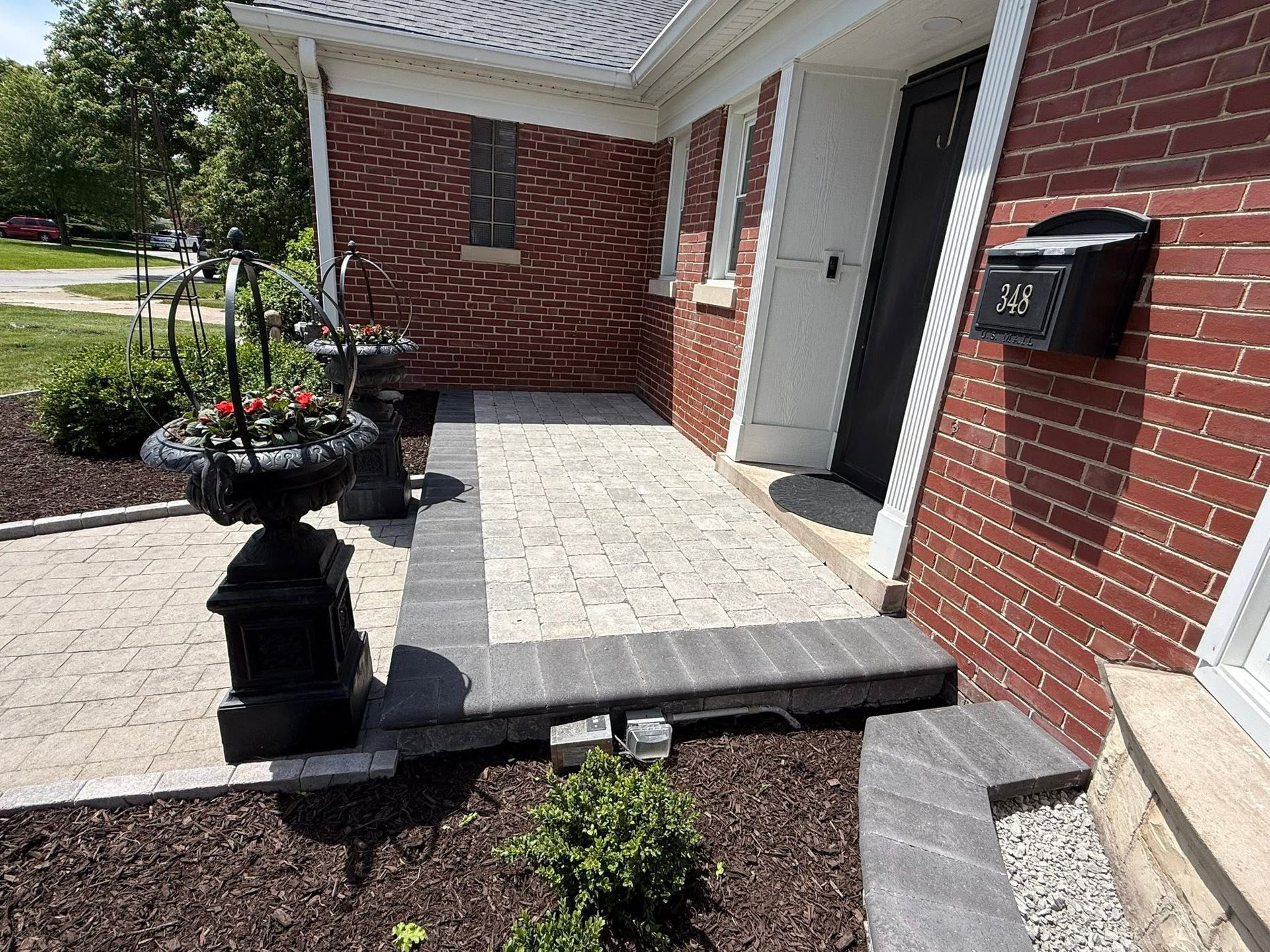 Brick house front entrance with tiled porch, steps, black planter, and mailbox by the door