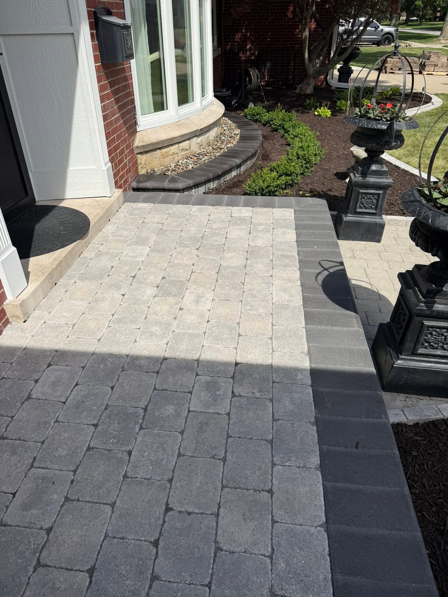 Stone patio and front entryway with pavers, a curved brick wall, and garden lights in sunlight