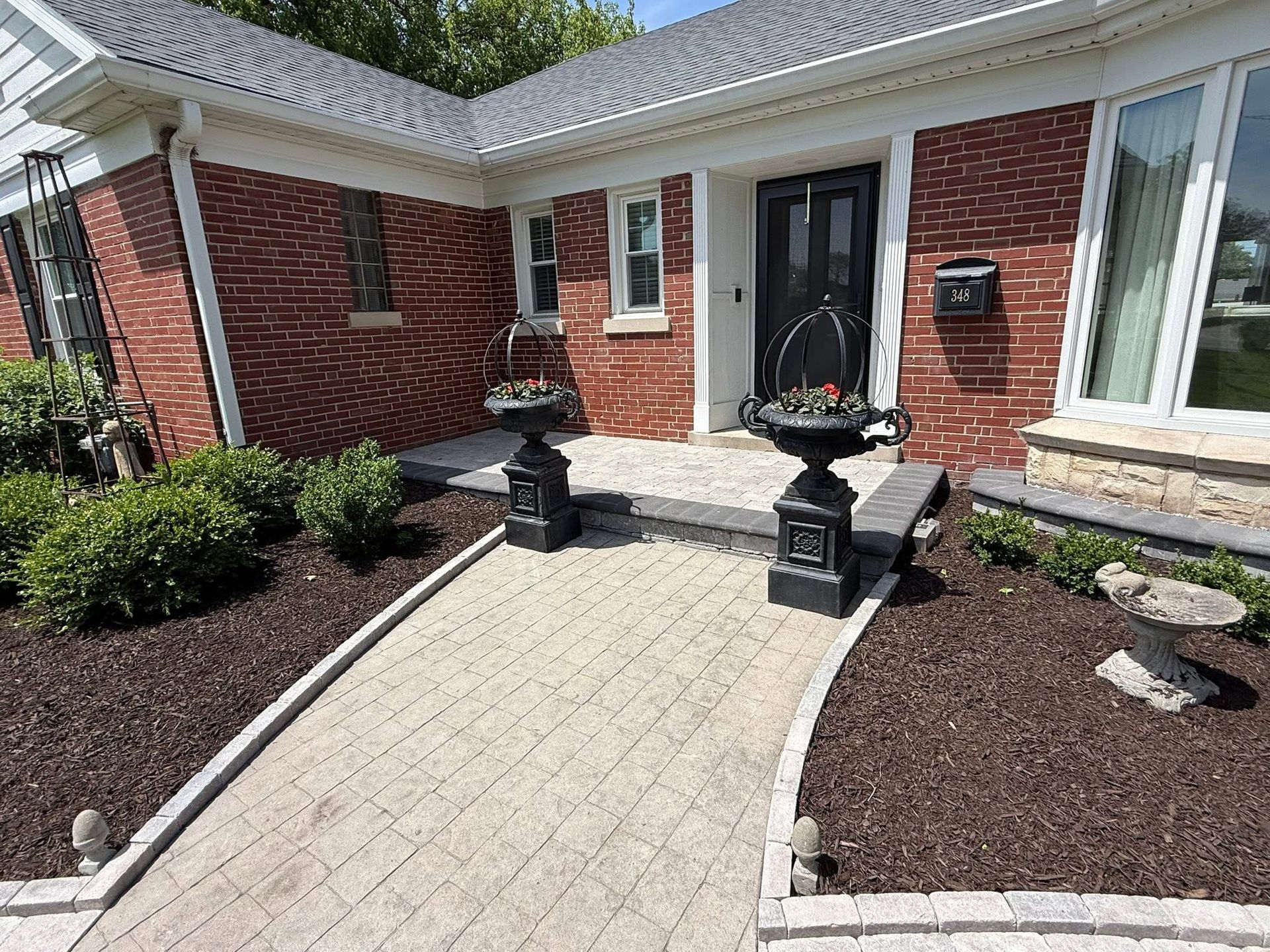 Brick house entryway with curved paver walkway, black planters, and landscaped beds