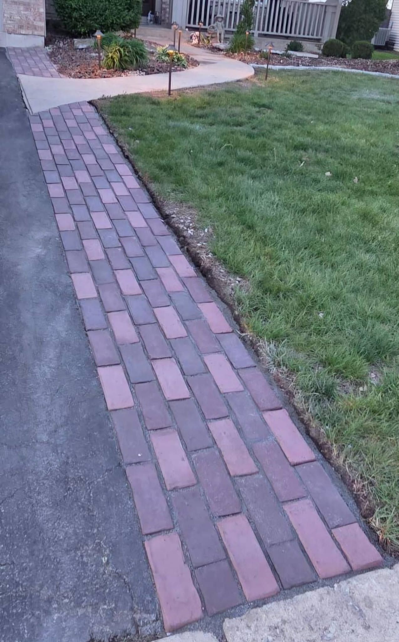 Brick walkway beside a grassy lawn leading to a patio and steps