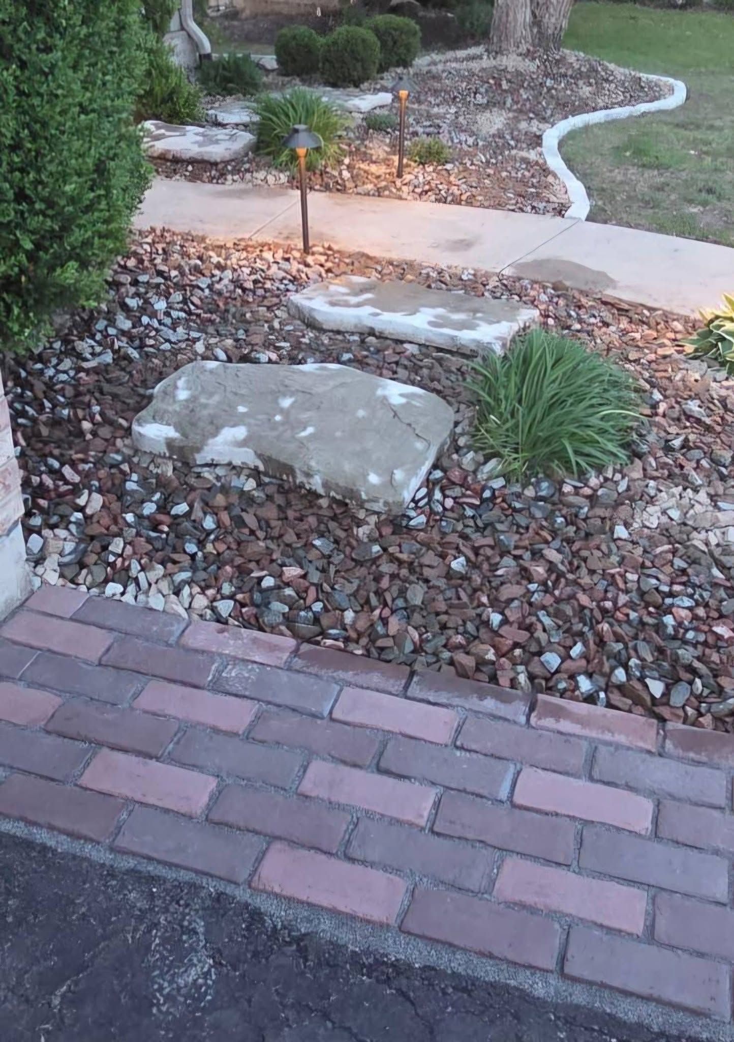 Brick walkway beside a landscaped garden with rocks, stone slabs, and shrubs