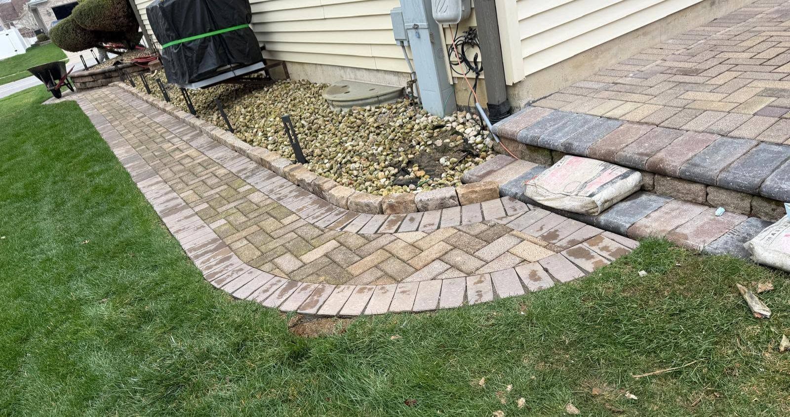 Curved brick walkway beside a house, bordering a small gravel bed and green lawn.