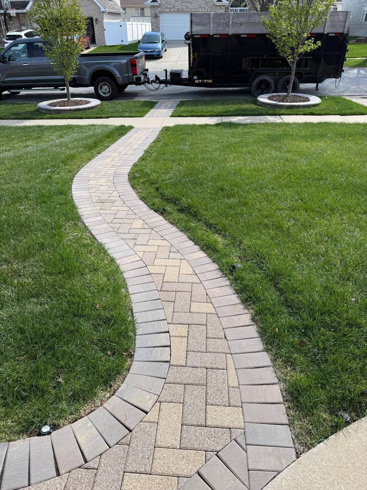Curved brick garden path through green lawn toward a driveway and truck in a suburban yard