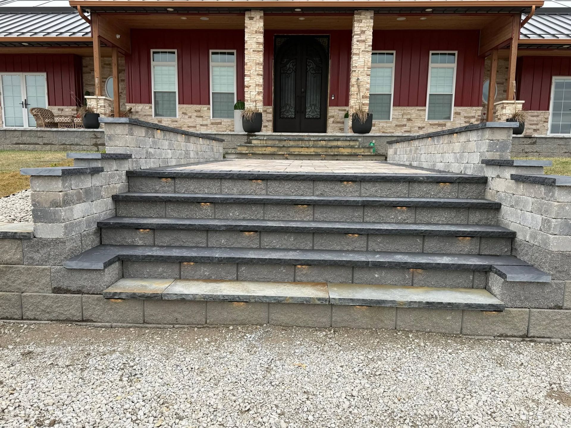 Stone steps leading to a red brick house with a black front door and stone porch railings