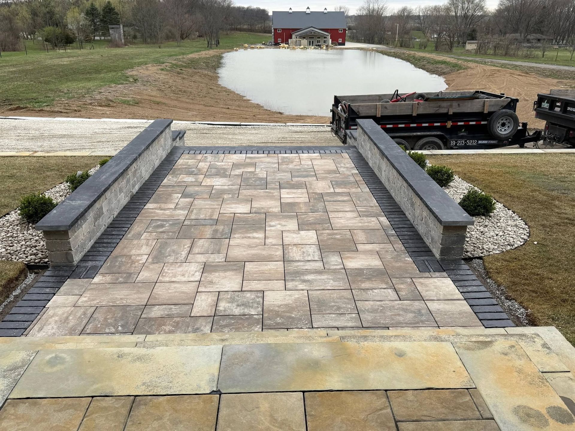 Stone-paved walkway with low retaining walls leading to a gravel driveway and red barn beyond.
