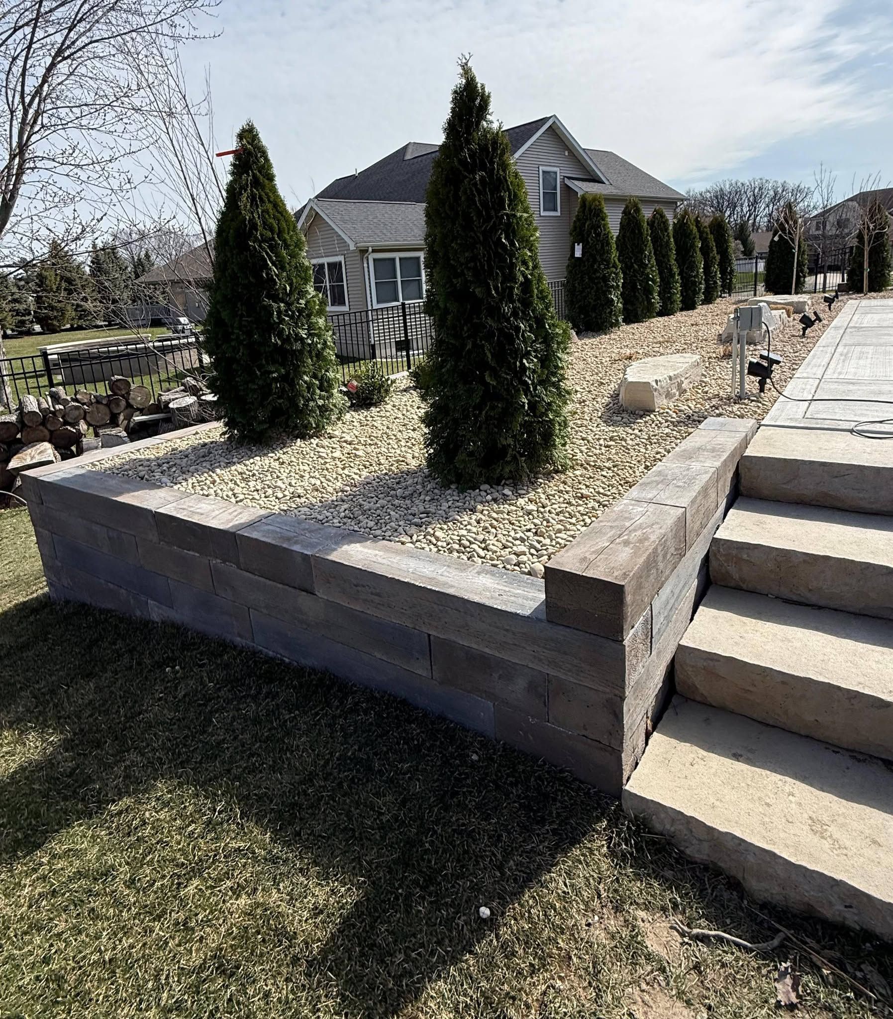 Raised stone planter with evergreen shrubs beside outdoor steps and a house