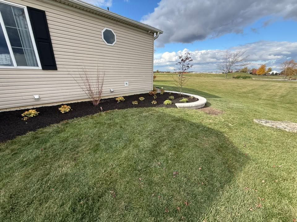 House siding with fresh mulch beds and a curved concrete walkway beside a grassy yard.