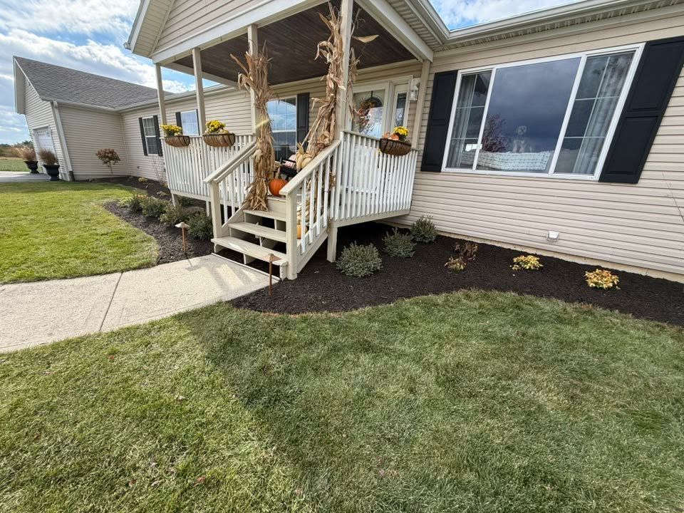 Front porch with white railings, pumpkins, and steps beside a beige house with a curved walkway and lawn.