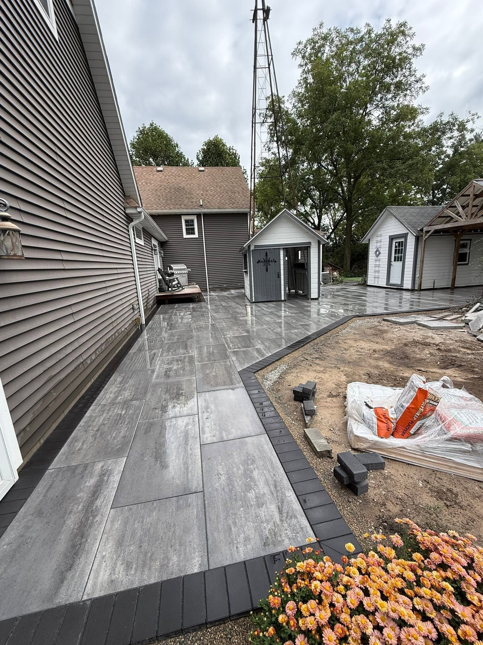 Narrow backyard patio with gray pavers, small sheds, and a gravel planting bed beside a house