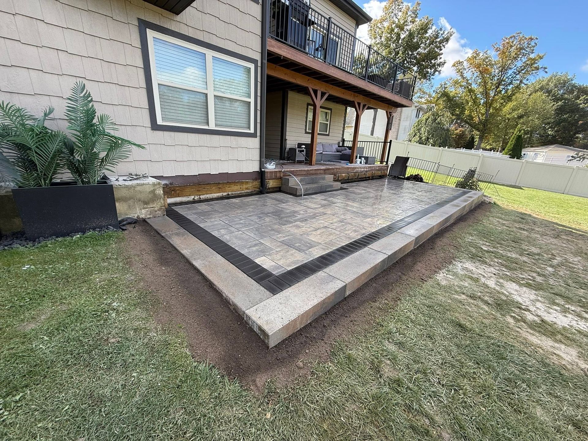 Backyard raised concrete patio with steps beside a house, bordered by grass and a fence