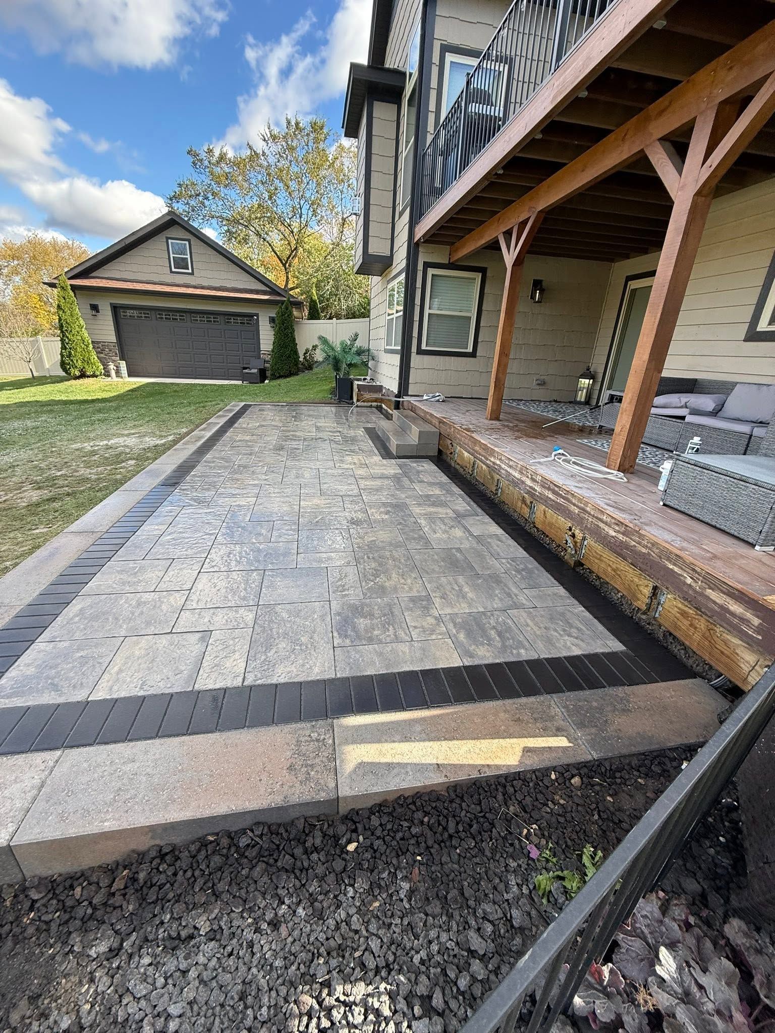 Stone patio path leading to a house porch, with a garage, lawn, and cloudy sky in the background