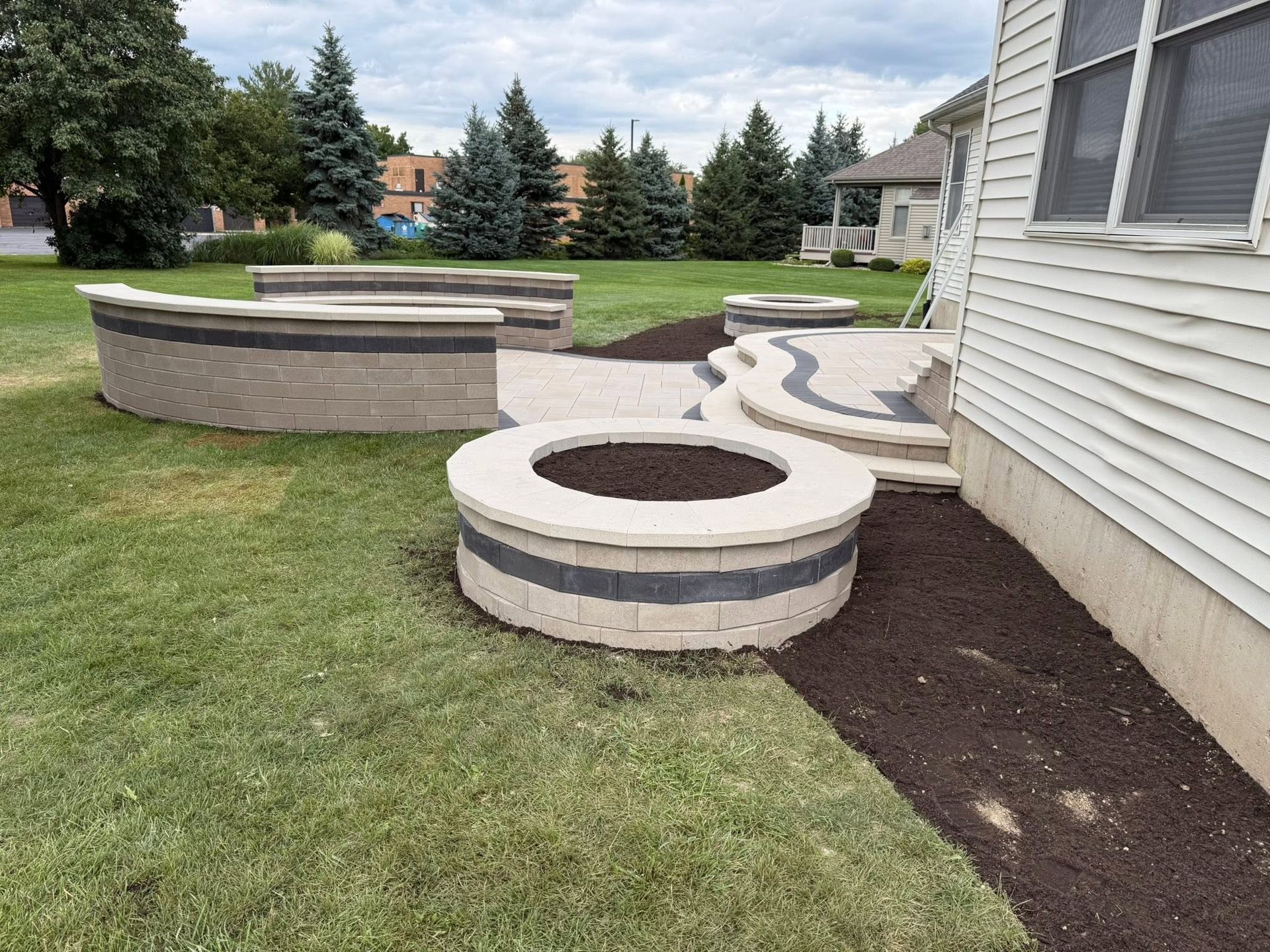 Landscaped yard with curved concrete planter walls and circular fire pits beside a house