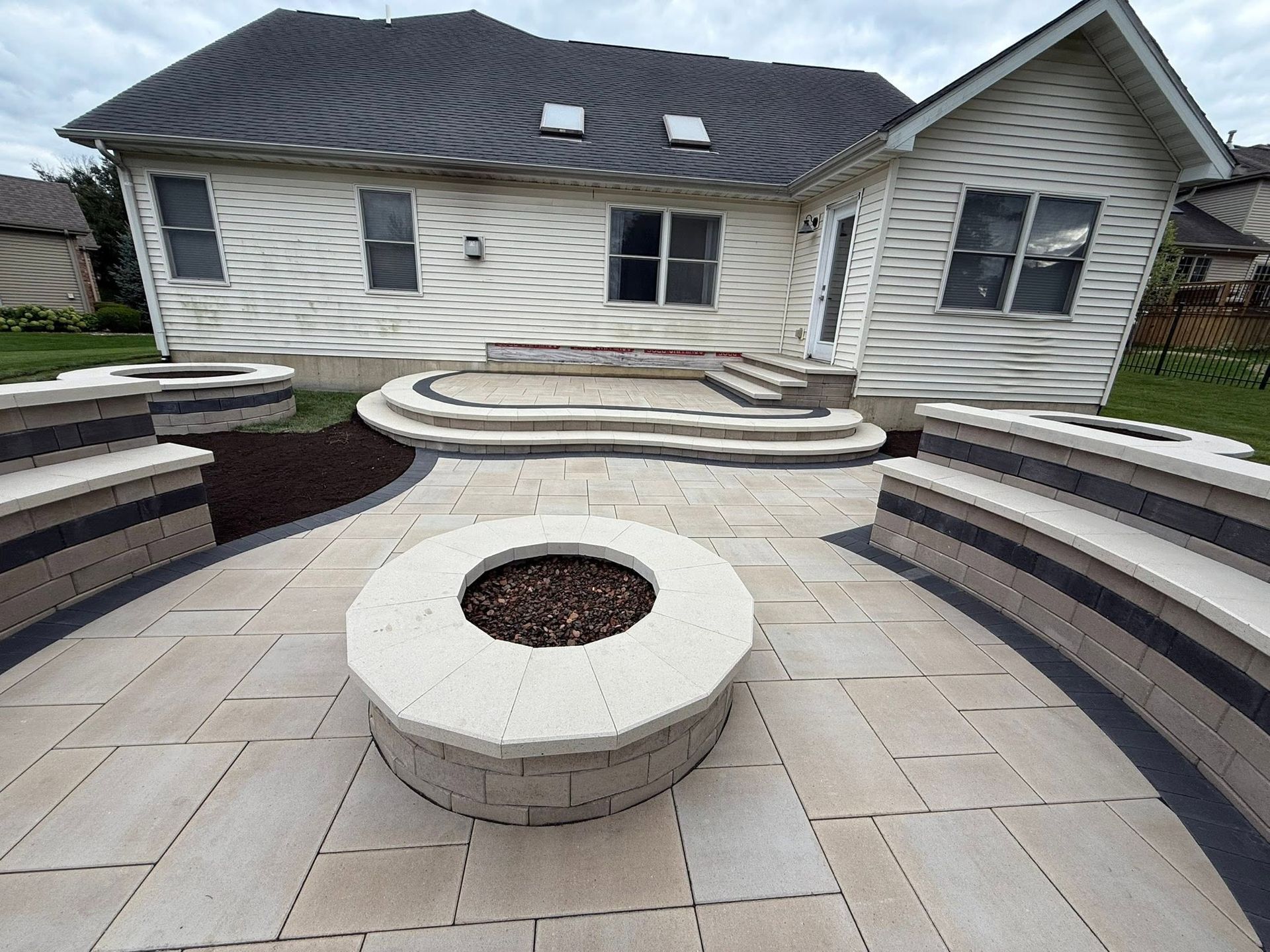 Backyard patio with curved stone seating, circular fire pit, and a house in the background