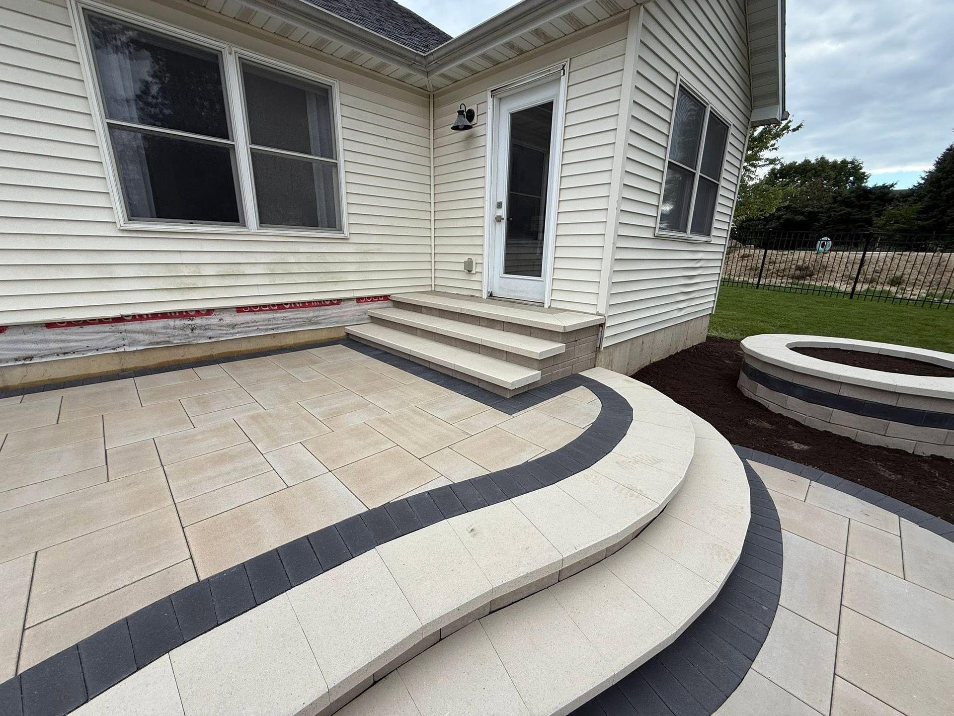 Curved concrete steps and patio leading to a white house’s side door and windows