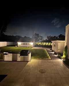 Nighttime patio with outdoor seating, lit lawn, and a house in the background