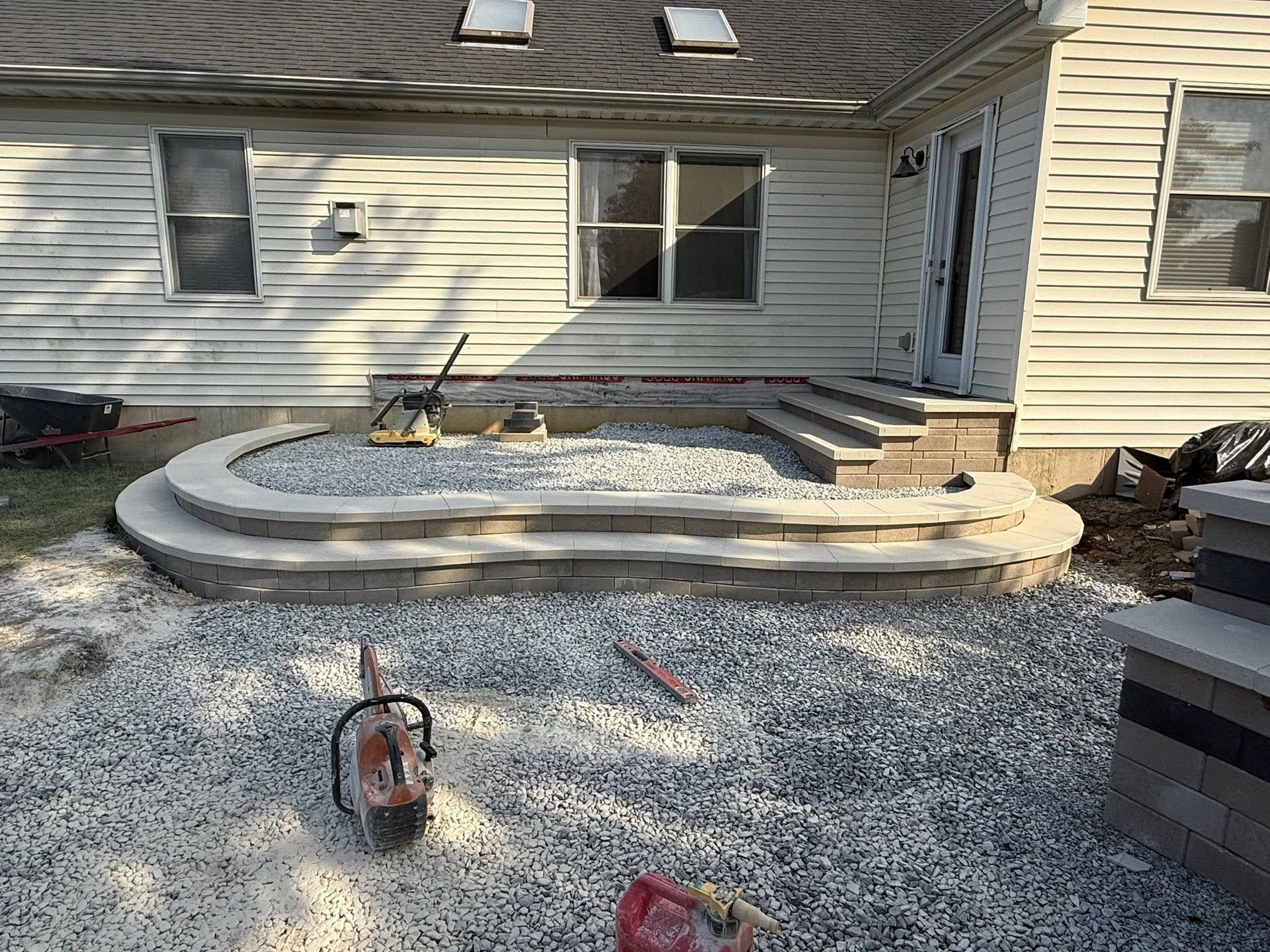 Backyard patio under construction with curved concrete steps and a gravel-covered ground
