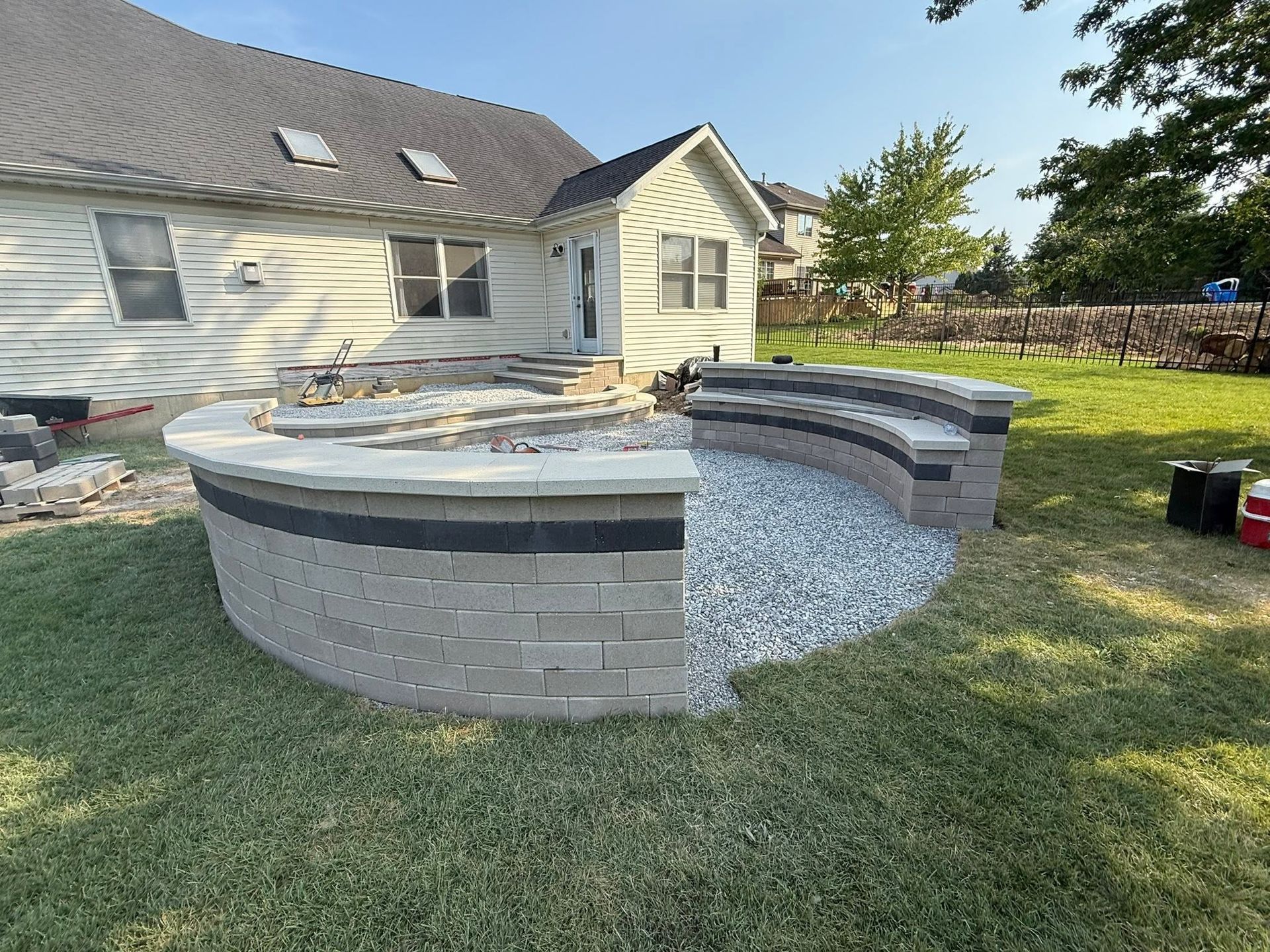 Backyard patio with curved stone seating wall and gravel fire pit area beside a house