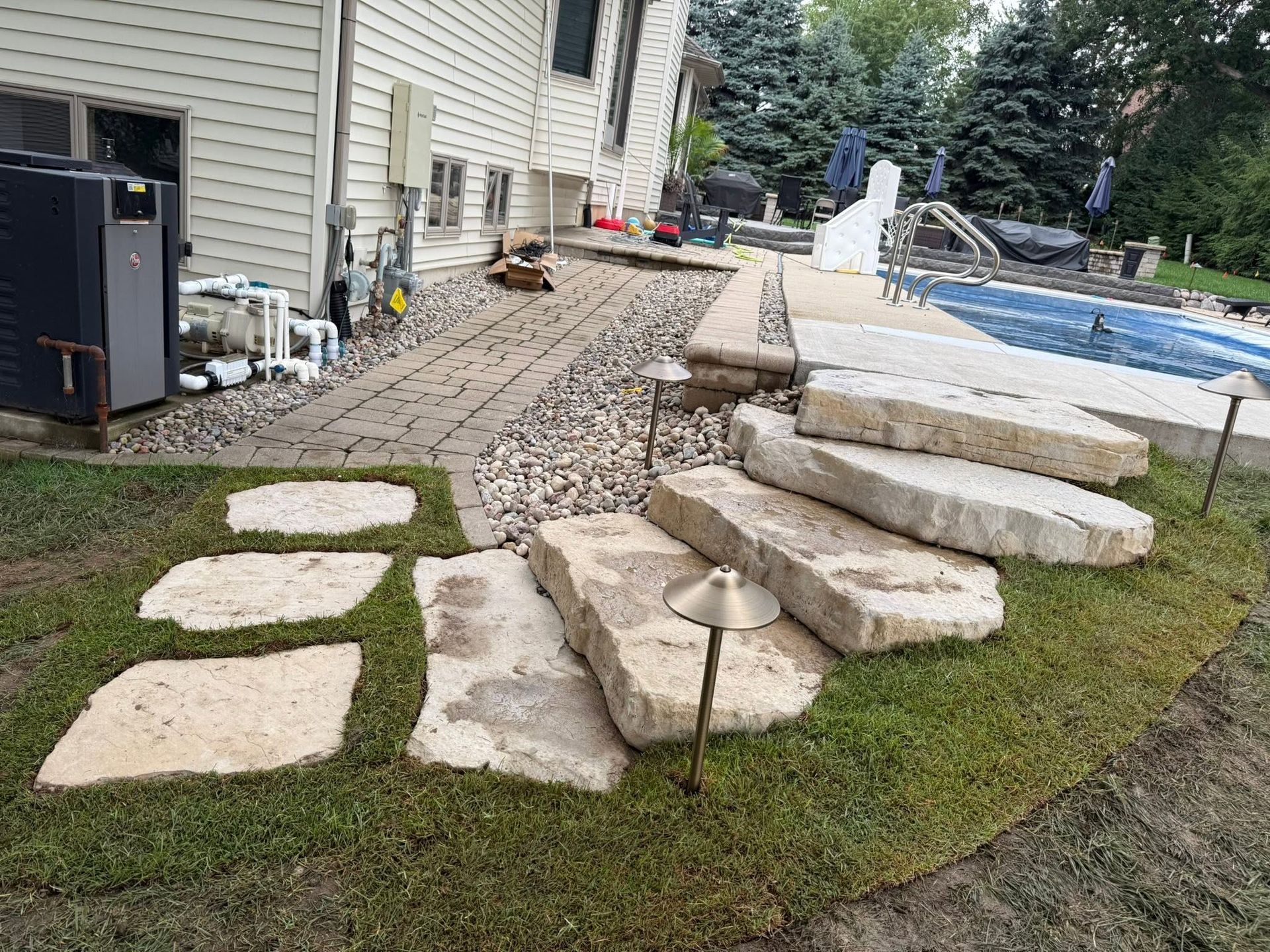 Stone patio and steps beside a house, leading to a backyard pool with lawn and pavers.