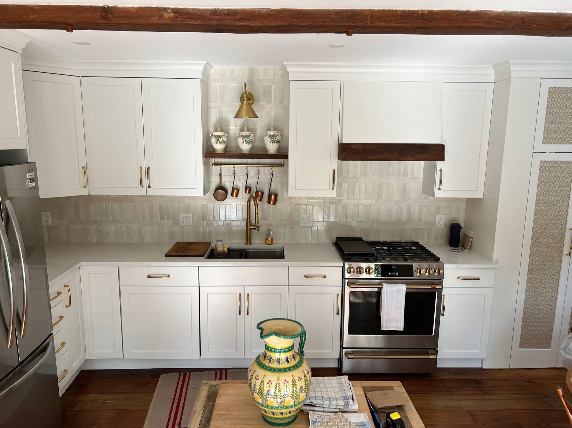 Modern kitchen with white cabinets, stainless steel appliances, and a wooden beam ceiling. A decorative yellow vase sits on the wooden island.