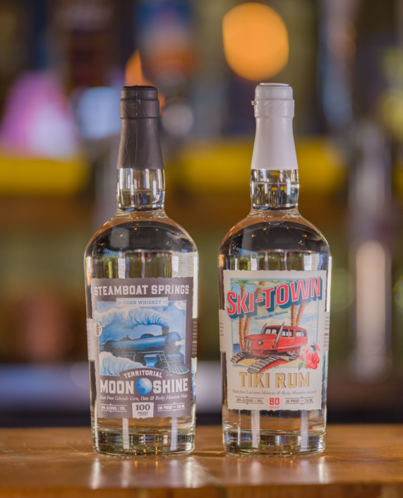 Two bottles of alcohol are sitting on a wooden table.