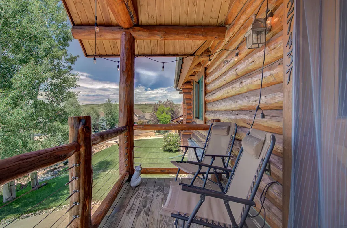 There are two rocking chairs on the porch of a log cabin.