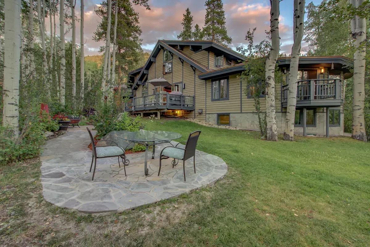A house with a patio area in front of it surrounded by trees.