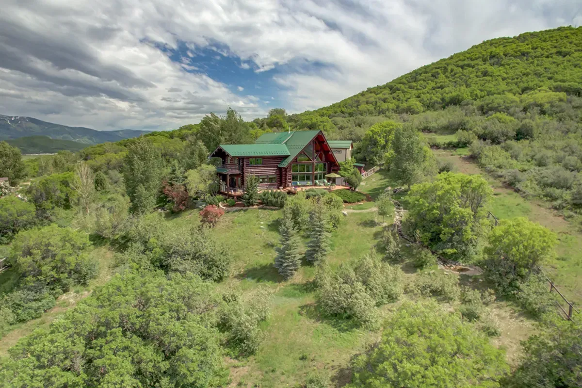 An aerial view of a house on top of a hill surrounded by trees.