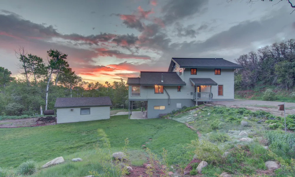 A large house is sitting on top of a hill with a sunset in the background.