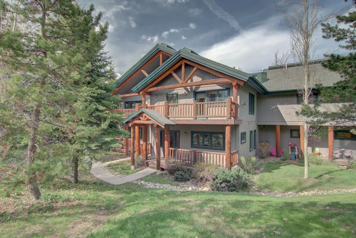 A large house with a green roof is surrounded by trees and grass.