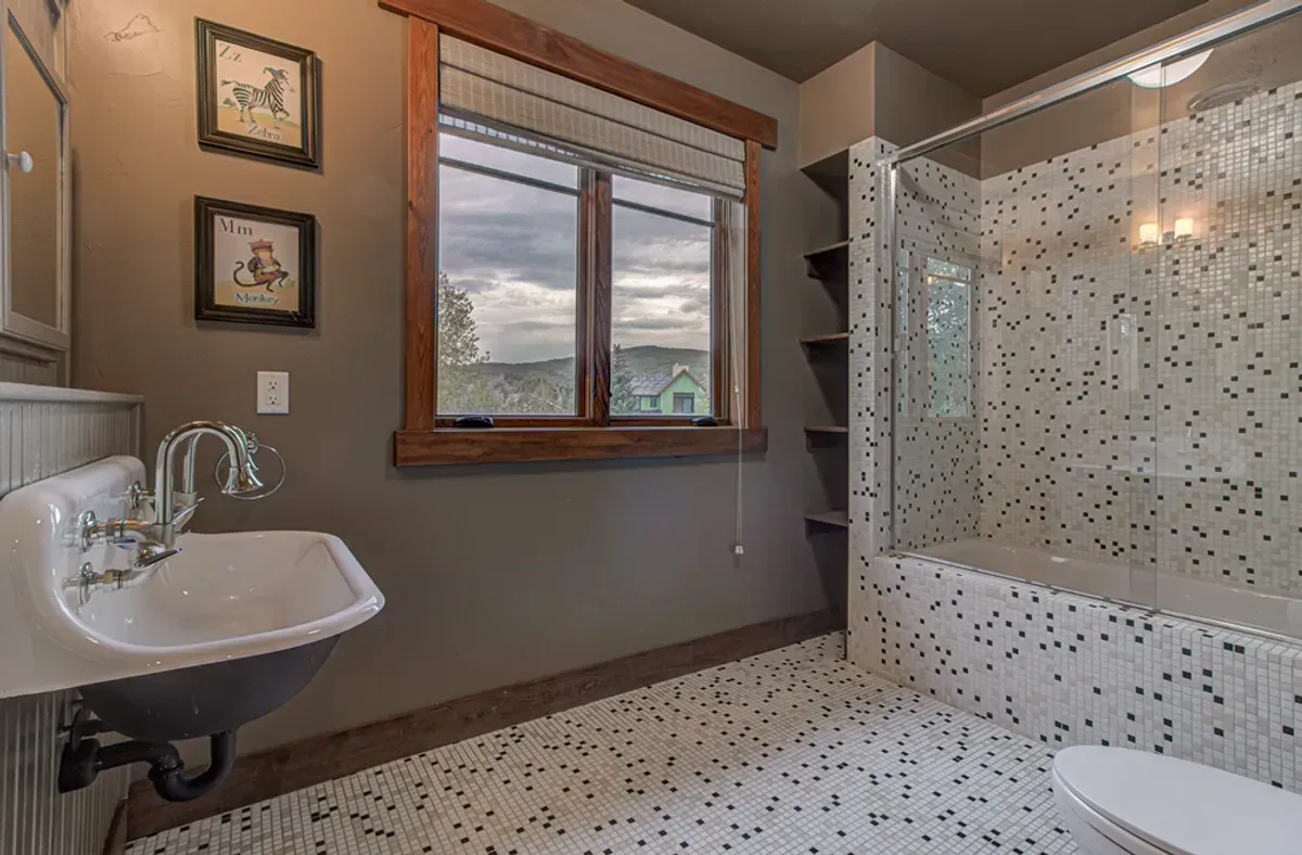 A bathroom with a sink , toilet , shower and window.