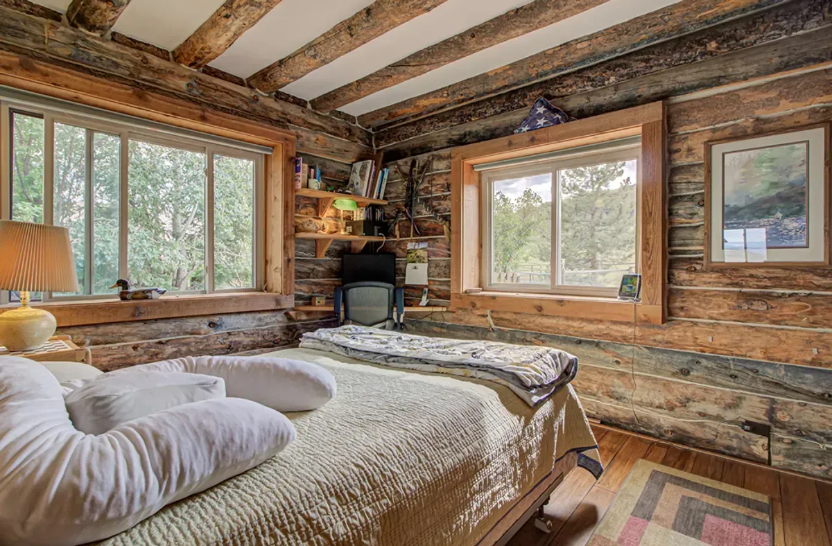 A bedroom in a log cabin with a bed and two windows.
