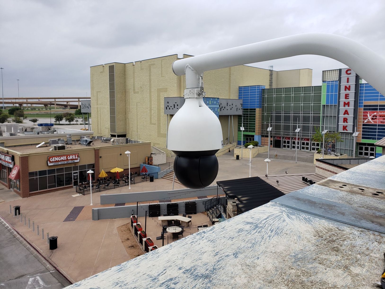 Close-up of a large white and black security camera overlooking a plaza and buildings Close-up of a large white and black security camera overlooking a plaza and buildings