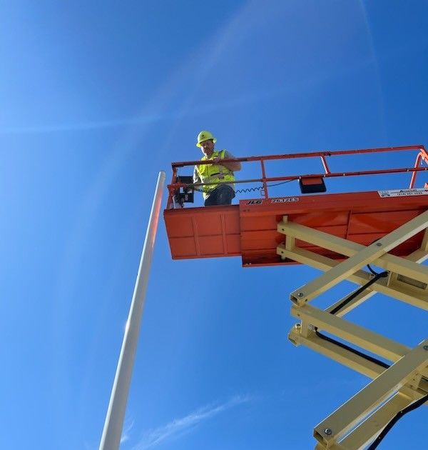 Worker in a high-visibility jacket standing on an elevated orange lift against a blue sky Worker in a high-visibility jacket standing on an elevated orange lift against a blue sky