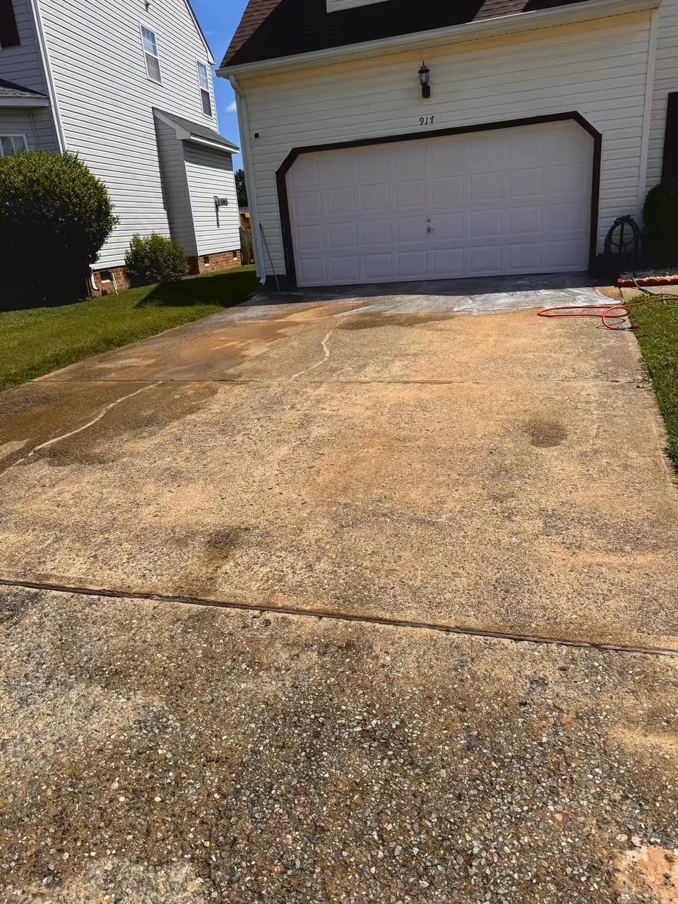 Driveway partially cleaned with a pressure washer; house with white garage door in background.