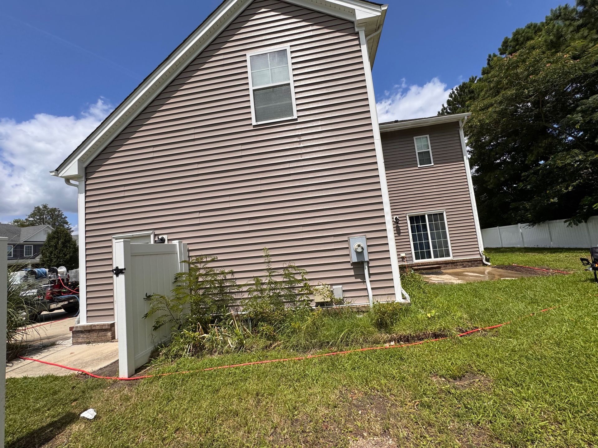 Side view of a house with brown siding, a fence, and a grassy yard on a sunny day.