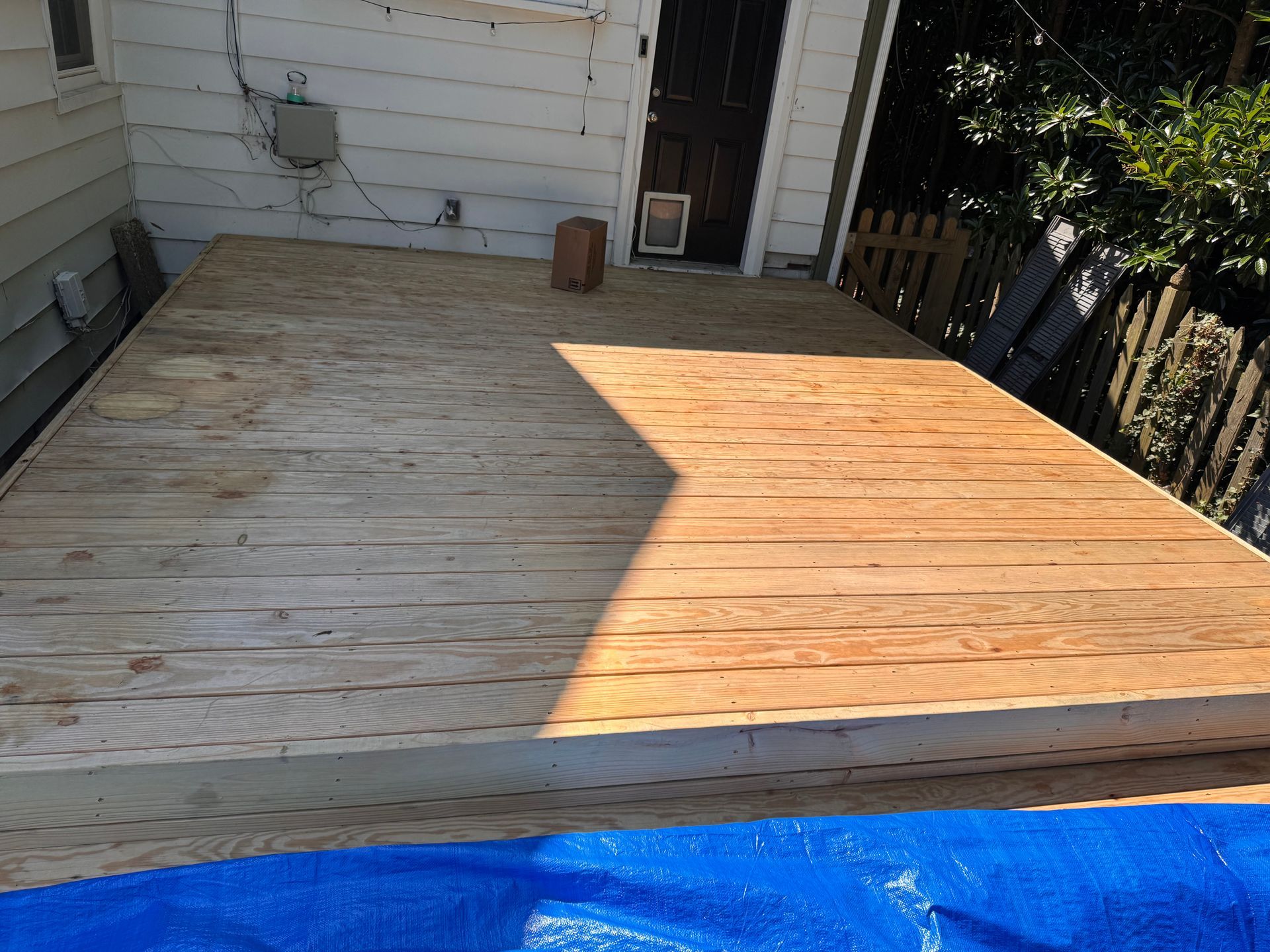 Wooden deck with weathered planks, back door, and partial shade.