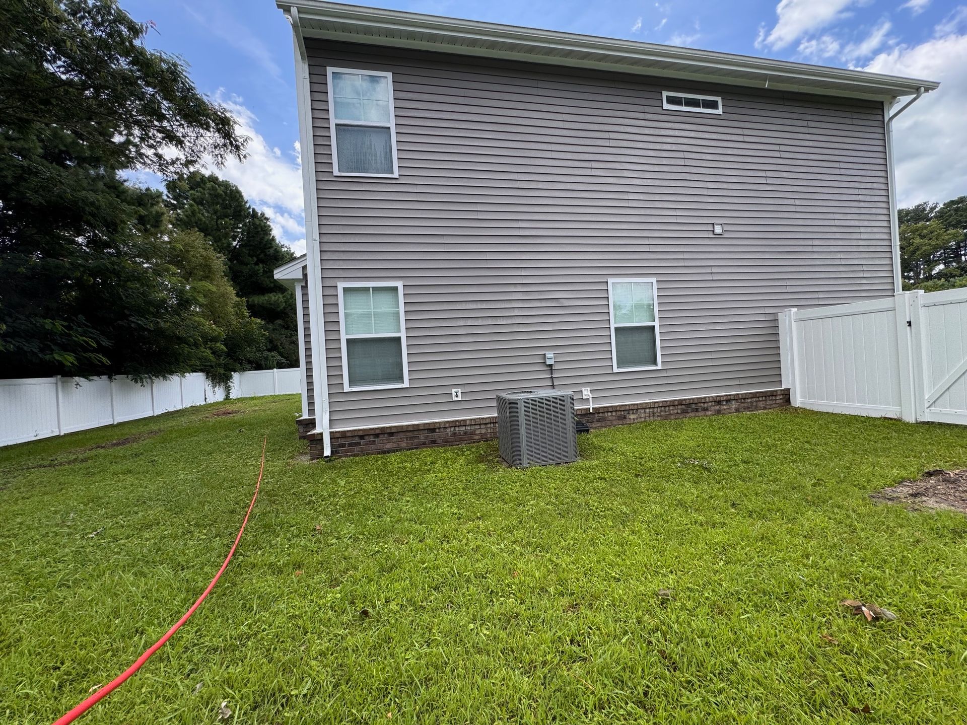 Backyard view of a two-story gray house with white trim, grass, and a white fence.