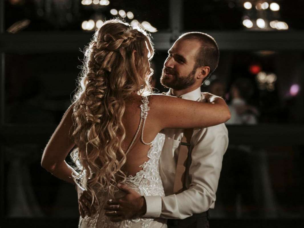 A couple in formal attire embraces during a dance, gazing at each other in a dimly lit, festive setting.