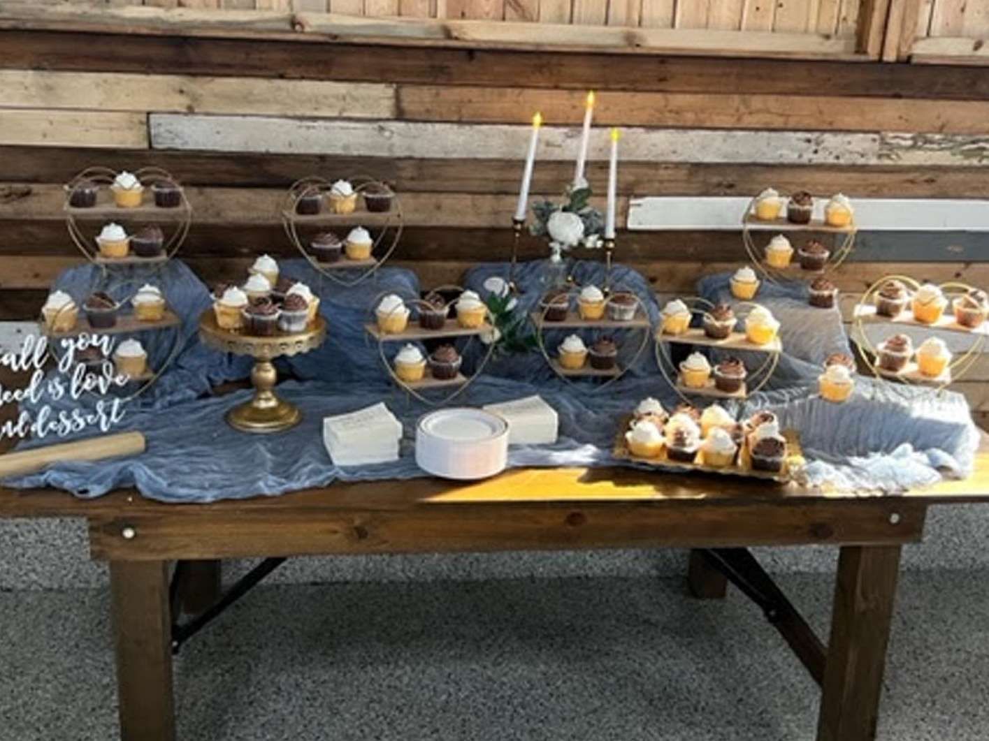 A rustic dessert table featuring numerous cupcakes on tiered stands and a wooden wall backdrop with candles.