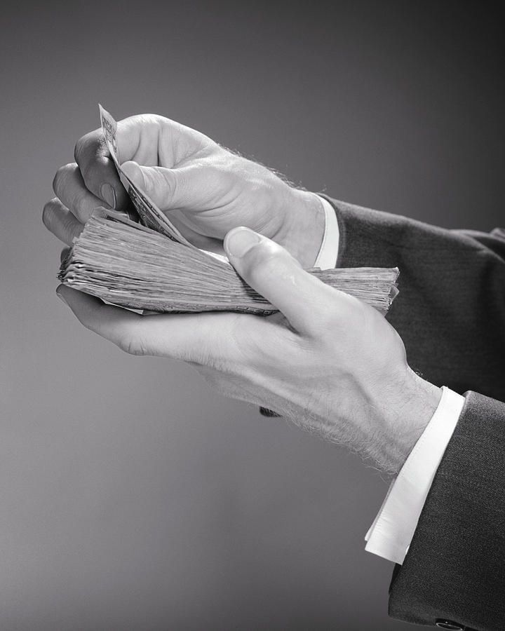 A person wearing a suit jacket counts a thick stack of paper currency.