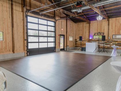 A rustic event venue featuring a large dark dance floor, wooden walls, a glass garage door, and audio equipment.
