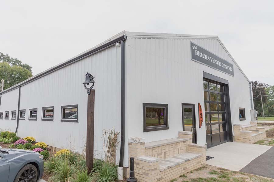 A modern white metal building with a large glass sectional door, dark trim, and decorative stone seating in front.