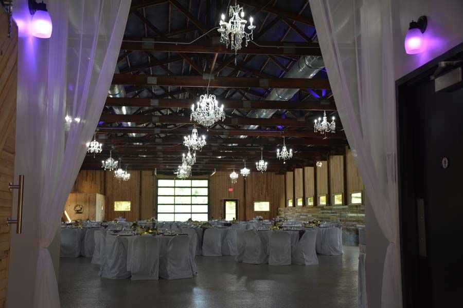 A large event hall with white-draped tables and chandeliers hanging from a high, dark wooden ceiling.