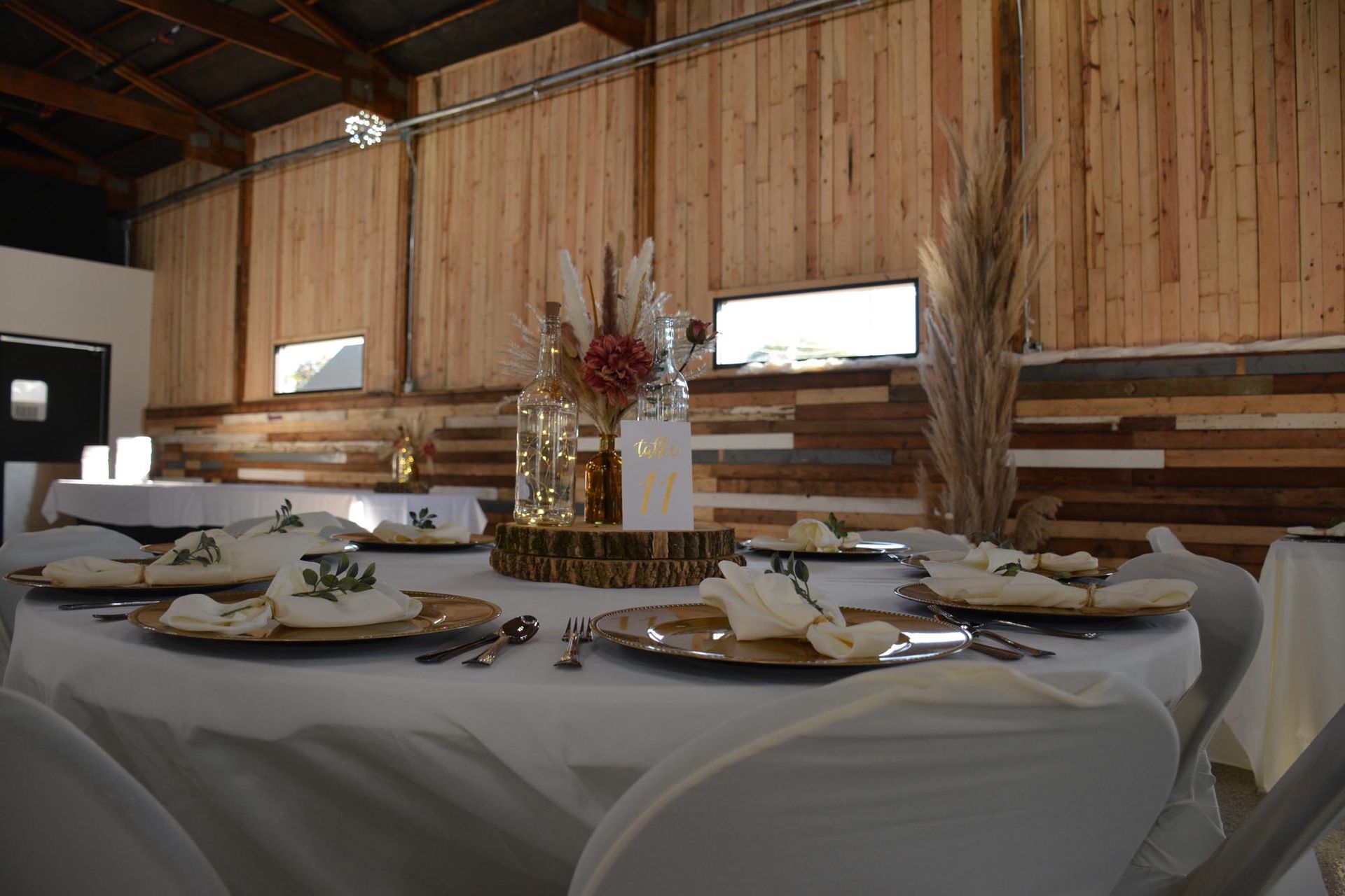 Round dining tables with white tablecloths and centerpieces inside a rustic event hall with wood-paneled walls.