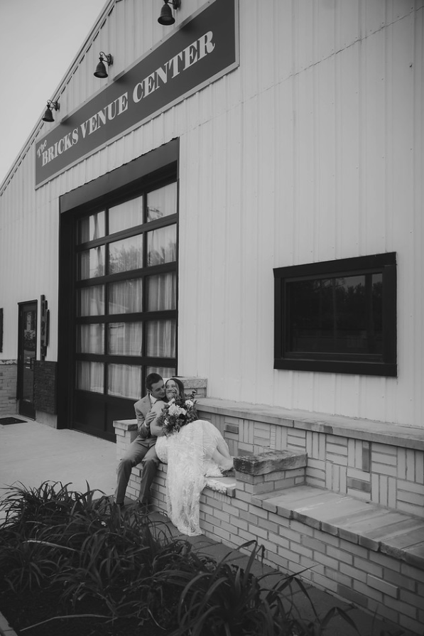A couple in wedding attire sitting on a brick ledge outside The Bricks Venue Center.
