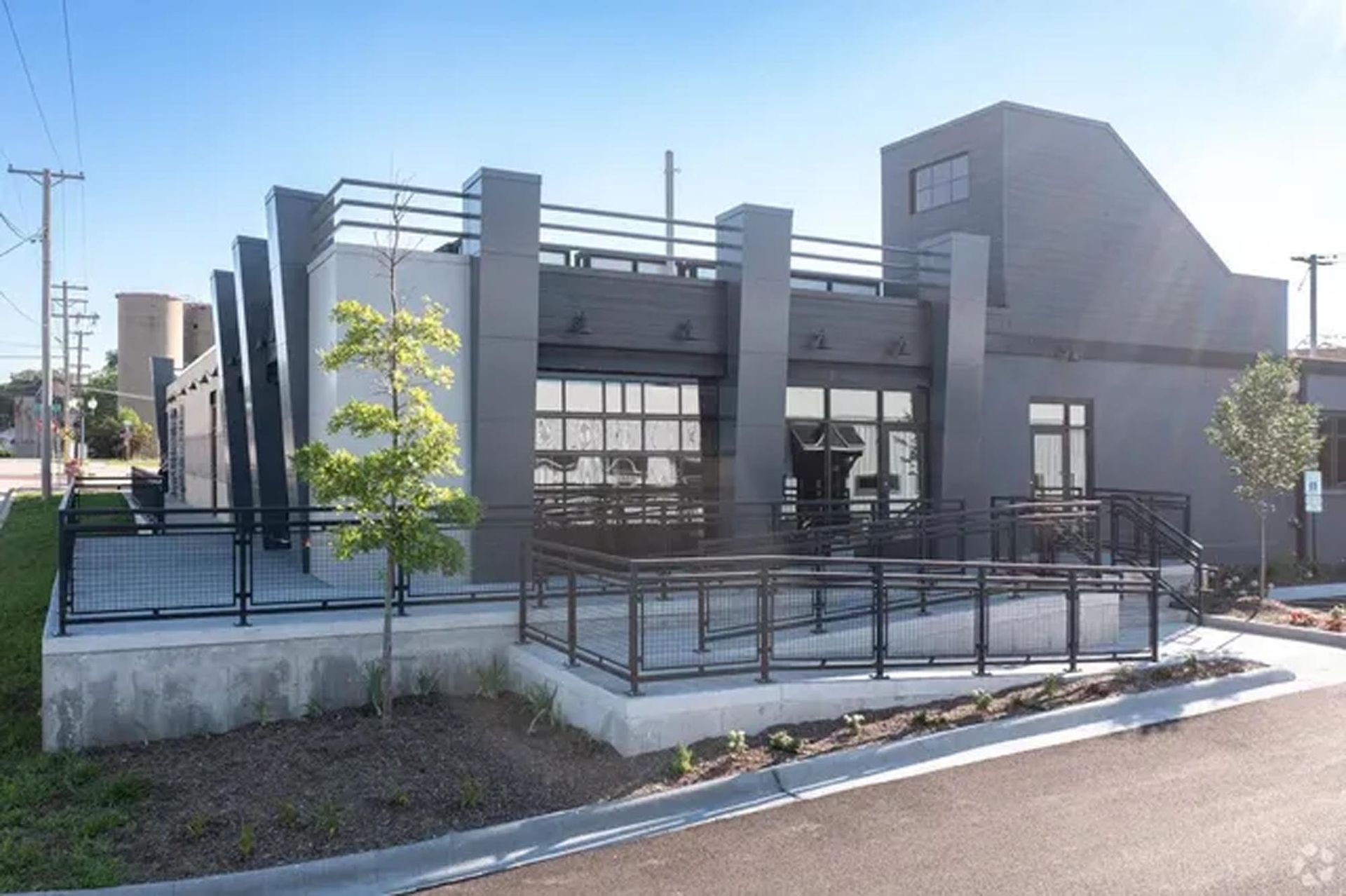 A modern, dark-gray commercial building with a roof deck, large glass garage-style doors, and a front wheelchair ramp.