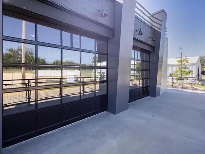 Modern industrial building with gray facade and large, glass-paneled garage-style doors opening onto a concrete patio.