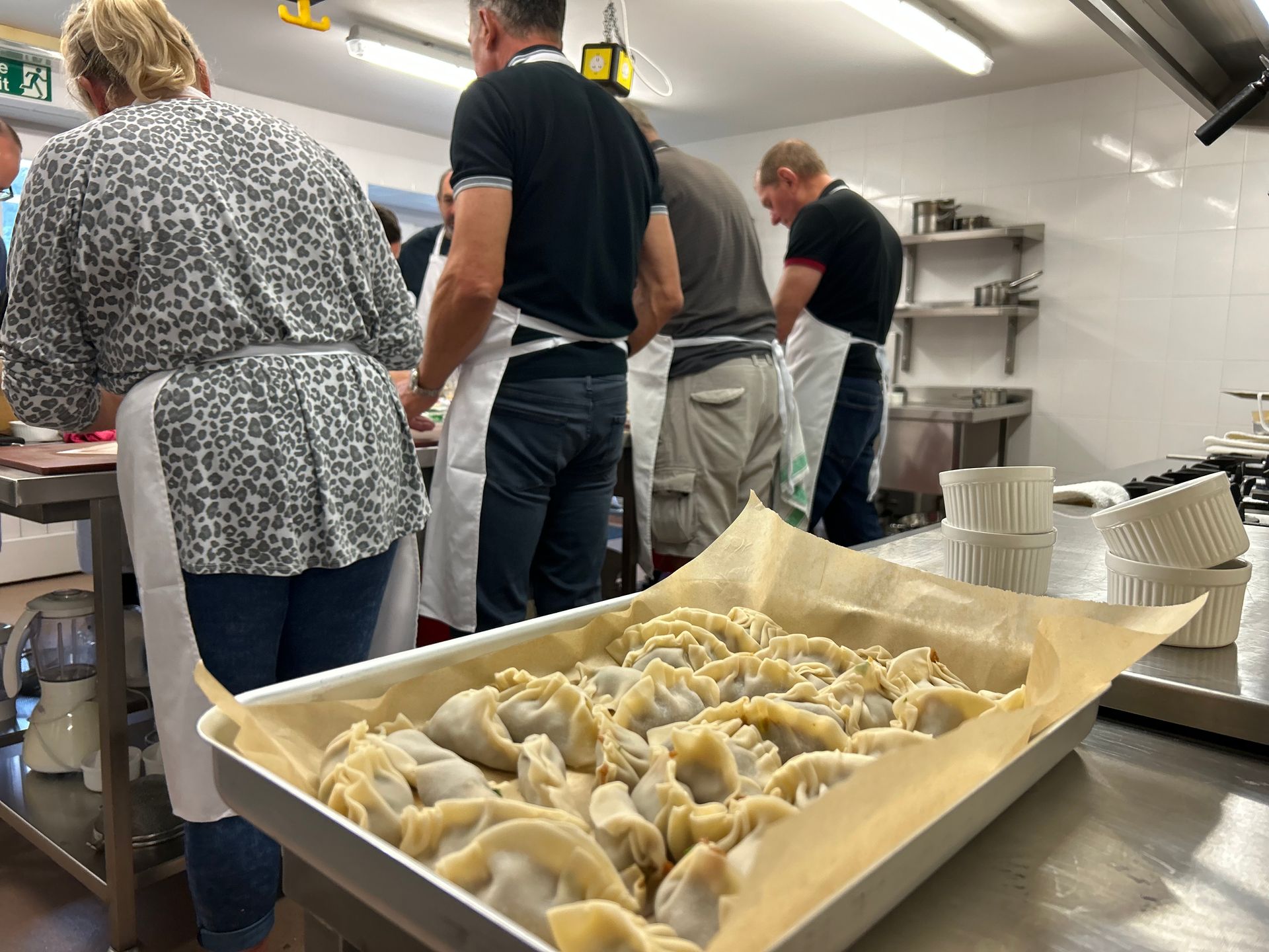 People in a kitchen making dumplings, a tray of them in the foreground.
